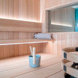 Moderni sauna sisustus, jossa näkyy SAUNA LED-valonauha, puinen penkki ja saunaämpäri.